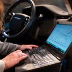 Engenheira usa um laptop para analisar dados de um veículo durante um teste técnico.
