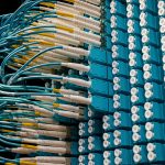 Cabos de fibra óptica conectados a um painel azul em um data center.