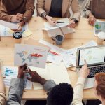 Equipe diversa reunida em torno de uma mesa, colaborando com laptops e gráficos em um ambiente corporativo