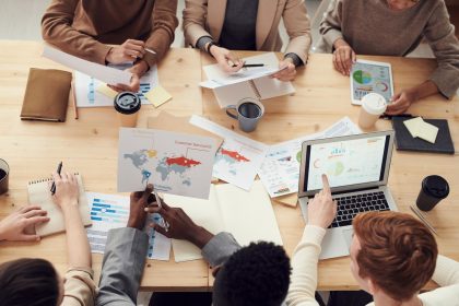 Equipe diversa reunida em torno de uma mesa, colaborando com laptops e gráficos em um ambiente corporativo