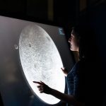 Mulher interage com uma tela que exibe detalhes da superfície da Lua.