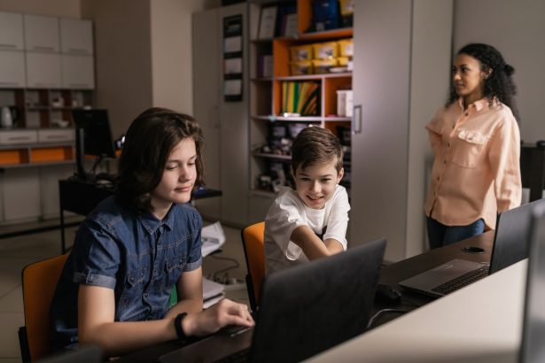 Estudantes usam laptops em uma sala de aula enquanto uma professora os supervisiona.