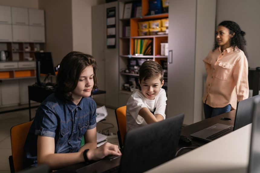 Estudantes usam laptops em uma sala de aula enquanto uma professora os supervisiona.
