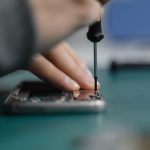 Mão usando uma chave de fenda para reparar um smartphone aberto.