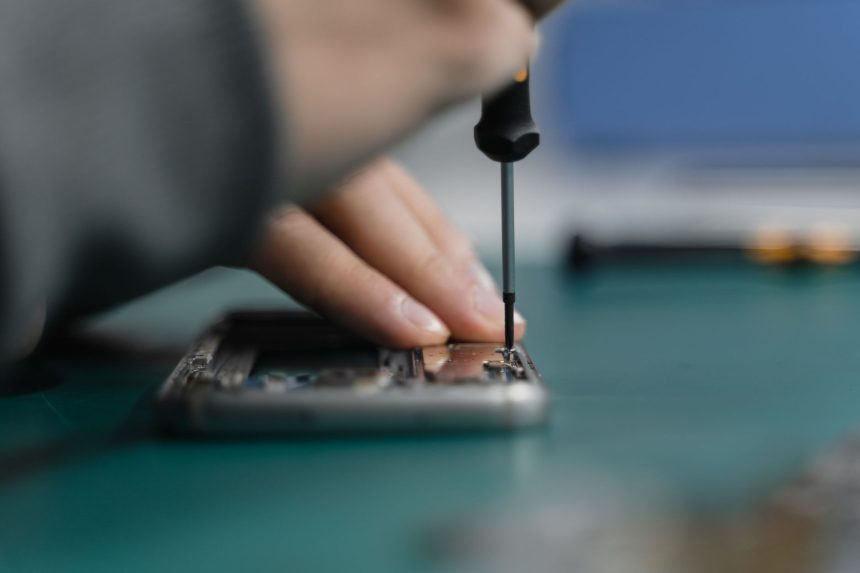 Mão usando uma chave de fenda para reparar um smartphone aberto.