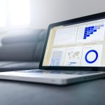 Notebook exibindo gráficos e painéis de análise de dados sobre uma mesa em ambiente de escritório.
