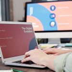 Pessoa usa um laptop em um escritório moderno diante de uma representação visual de evolução digital e inteligência artificial.