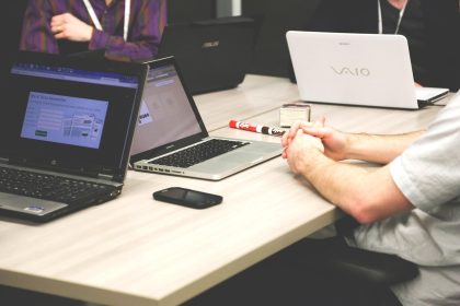 Grupo de pessoas reunido em torno de uma mesa com computadores durante uma discussão de trabalho.